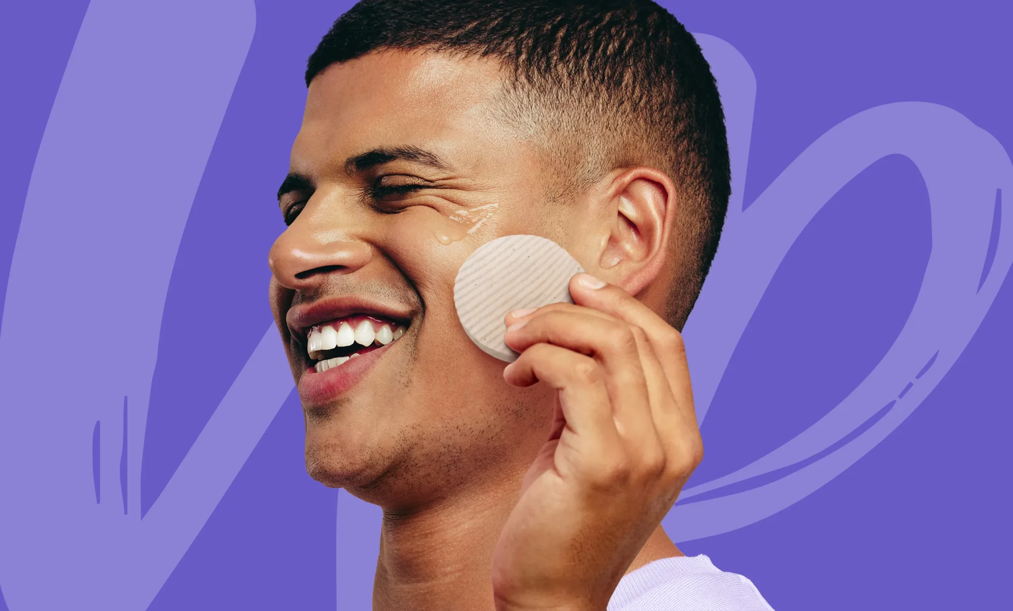 Chico joven y moreno, muy sonriente, probando los productos de DEMAKUP sobre un fondo azulado. Campaña realizada por Playroom 306º