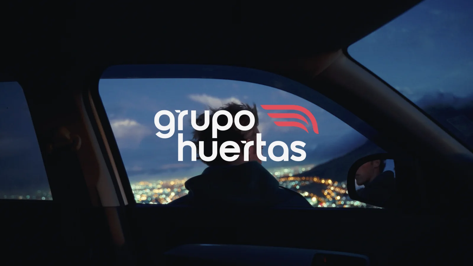 fotograma nocturno desde el interior de un coche con las luces de la ciudad al fondo y el logotipo de Grupo Huertas